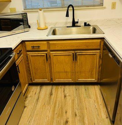 Installed flooring, kitchen counter, sink, faucet, and cabinet hardware.