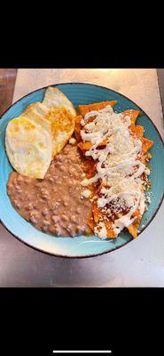 Our breakfast specialty, Red Chilaquiles with fried eggs and refried beans, topped with sour cream and queso fresco