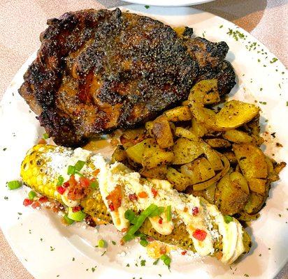 Shown here is 16 oz Flame Grilled Ribeye Steak (over oak logs), with Fire Corn and Potatoes w/ Onions