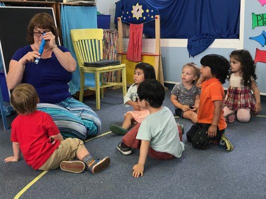 Toddlers curiously looking on as their teacher engages them in story time.