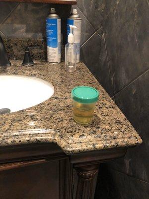 Random pee cup with no label sitting out on counter in bathroom.