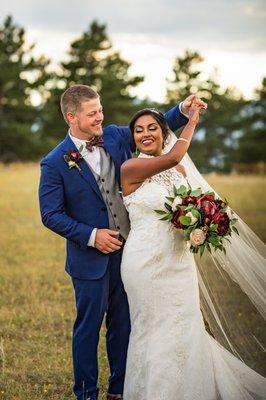 A groom twirling a bride in a field as she holds her bouquet