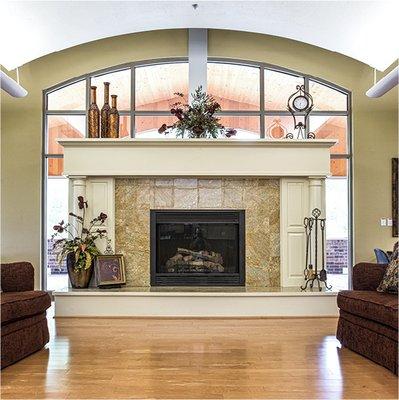 Great room of senior living community in Green Bay Wisconsin with a large fireplace with windows behind it and two beige sofas in front.