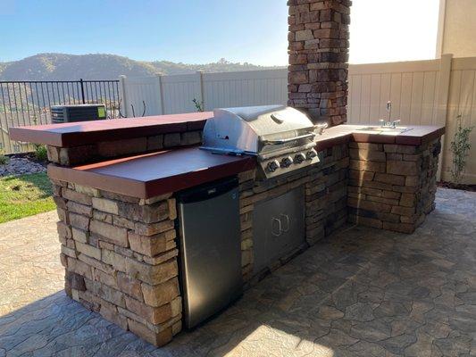 BBQ Island and bar with concrete countertop, veneer stone, mini-fridge, burner, grill, access door, sink, and LED lights