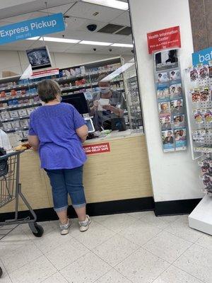 Member of management with mask pulled down below nose working the pharmacy.