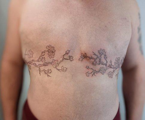 Mastectomy scar coverup tattoo: linework of a cherry blossom branch extending from under each arm, nearly meeting in the middle.