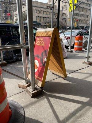 New York City architecture surrounds this beautiful sidewalk sign.