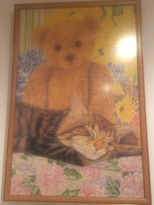 A framed puzzle  " A relaxed cat and it's teddy bear on the couch"