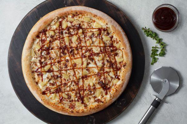 Barbeque Chicken Pizza, made with fresh dough, barbeque sauce, cheese, chicken, bacon, pineapple & drizzle of BBQ sauce on top