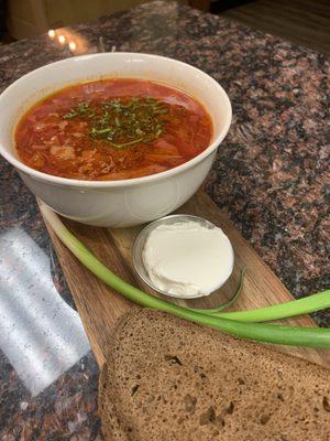 Traditional borscht on a wooden board, with green onions, sour cream, and dark rye bread--delicious, hearty, and homestyle!