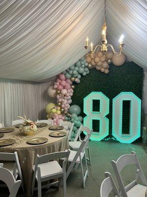 Tent, drapes, chandelier, backdrop, center pieces, table cloth, plates, table runner, chairs,  and lighted numbers.