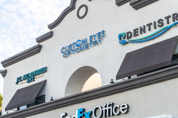 Close-up of Custom Eyes Optometry's logo and building signage above the storefront in Costa Mesa, CA.