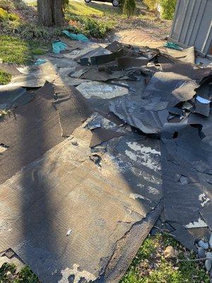 Old roofing material left on the front yard overnight, with no sign of insulation boards because it was improperly reused for the new roof.