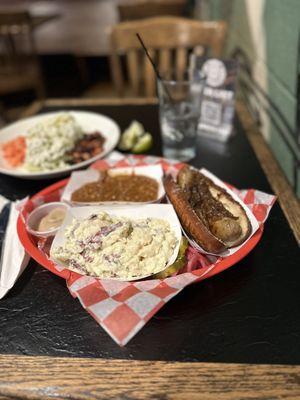 Bratwurst on a toasted pretzel bun with caramel onions, potato salad and amazing baked beans