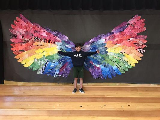 A student posing in front of one of our collaborative, school-wide, art installations at the annual art show!