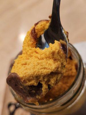 A spoon pulls out a spoonful of the Chocolucma dessert from the glass jar from where it was served.