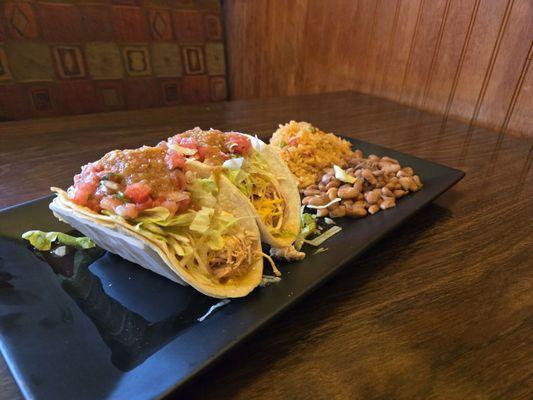 Two chicken tacos with sides of rice and whole pinto beans