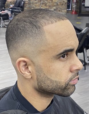 Mid-to-high skin fade that's faded into a shaped up full beard.