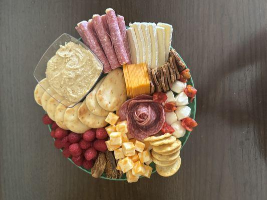 A charcuterie board with hummus, cheese, figs, a salami rose, and crackers.