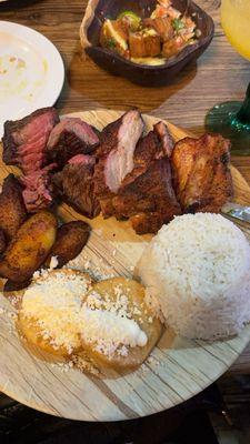 Mixed Plate (Beef and Pork Ribs) with white rice, arepitas, and Sweet Plantain; in the back Chicharrón Ceviche