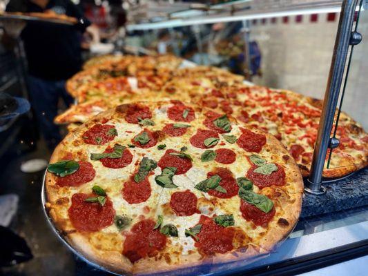 Pizza options seen through storefront window. Little Italy Pizza, New York.