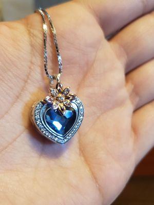 Front of necklace. Silver heart, with blue stone in the middle, and a rose gold lotus flower on top of the heart. Her remains are inside