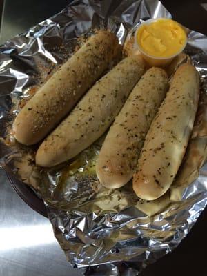 A delicious order of garlic breadsticks with cheese dipping sauce.