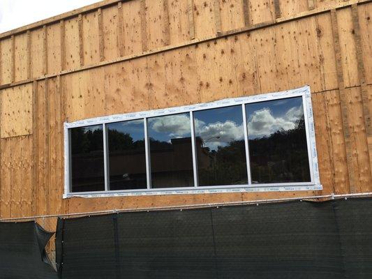 Installation of storefront window panels with mill clear anodized finish on wood framing.