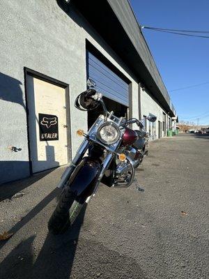 Suzuki motorcycle with new tires in front of shop door.