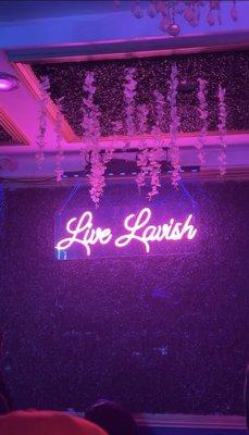 Neon sign on grass covered wall. Flowers hanging from ceiling