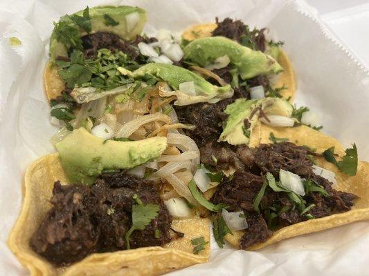 Barbacoa street tacos with avocado and grilled onions on the side.