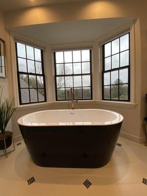 Focal point tub in gorgeous bay window with black windows highlighting the black details in the bathroom.