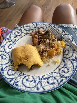 Half eaten plate of beef patty, jerk chicken, peas and rice, and cabbage