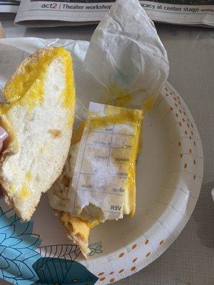 An egg sandwich with cheese AND A PIECE OF PAPER on a roll.