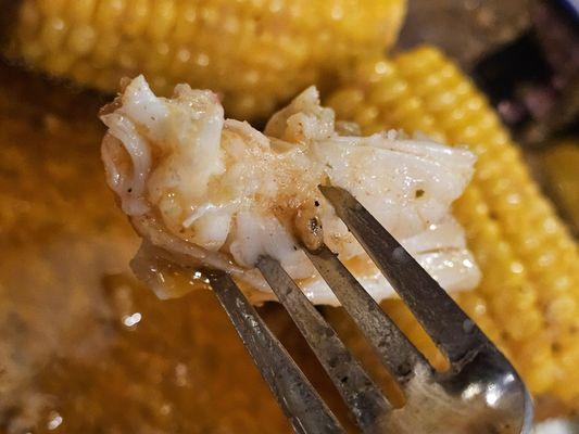 A fork holding a piece of the Lobster Tail meat with the Corn on the Cob in the background.