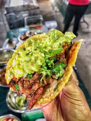 Signature Prime Cut Beef Taco on a Handmade Yellow Corn Tortilla garnished with a blend of chopped onion/cilantro and topped with Guacamole