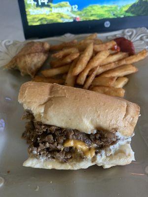 Half of a cheesesteak with cheese whiz, crab cake egg roll and seasoned fries with mambo sauce.