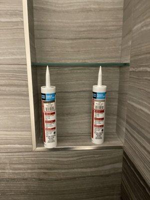 Matching grout for tiles, 2 colors of tile and grout. Shelves have a gap at the back for water to drain. Metal trim around tile edges.