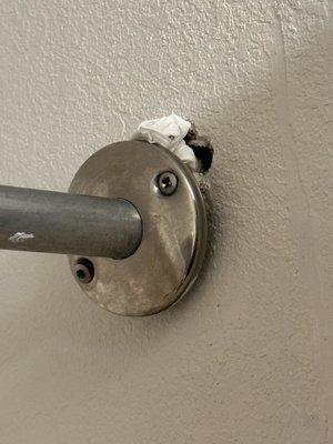 Shower rod hanging by one screw with trash stuffed in the hole