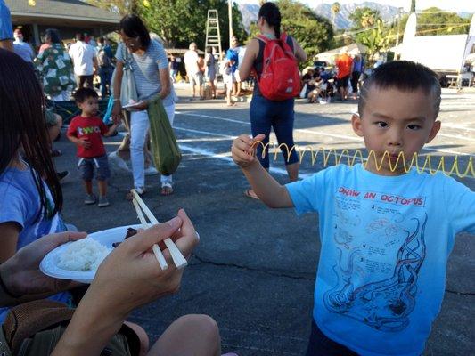 my son enjoying some teriyaki rice and toys from a booth at Obon