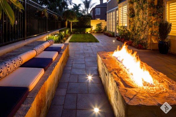 Paver installation with custom paver seating bench, natural stone fire pit and ambient outdoor lighting.