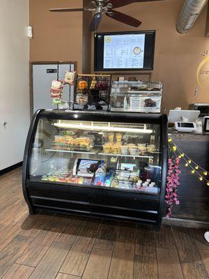 A warm welcoming shop featuring a pastry cabinet with a digital menu above