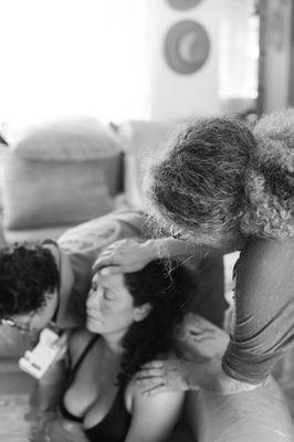 Mother supporting her daughter in labor, while the midwife is checking on baby