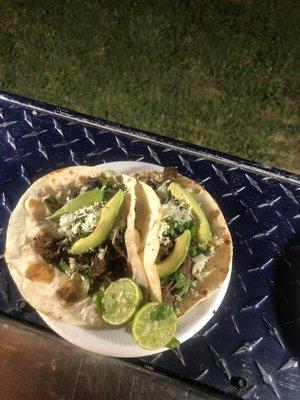 Carne asada tacos topped with onion, cilantro, queso fresco and avocado slices