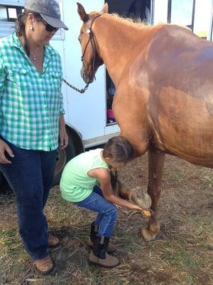 A young cowgirl learning how to care for her horse after her lessons. Picking the horses hooves after riding is important.