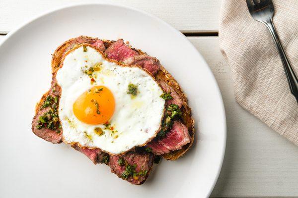 Our Chimmy Steak Toast is topped with a 6oz filet, sunny side up egg, Chimichurri sauce, and your choice of a side.