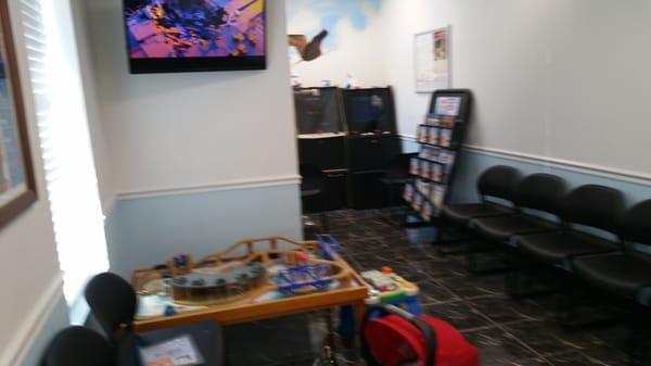 Waiting area for "well" patients has 2 arcade style games, a playstation and wooden train tracks for kids.