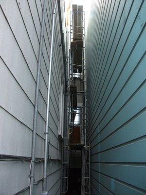 Scaffolding installed to replace long drain pipe on outside of building (on left at back of building).