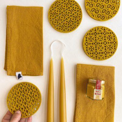 Gold Tones Flat Lay: Akakpo & Co Coasters, Amphitrite Studio Napkins, Danica Candles, Raye's Mustard