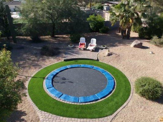 Artificial turf ring around a sunken trampoline.  Paver border on both sides and raised paver patio.